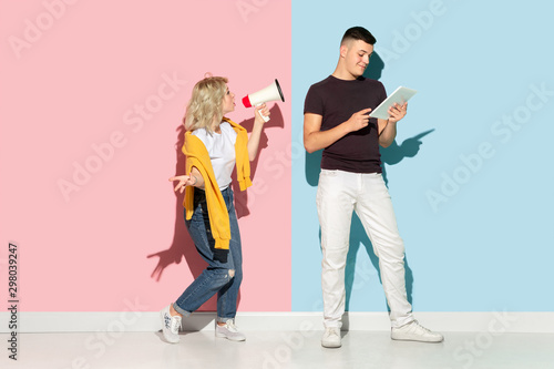 Young emotional man and woman in bright casual clothes posing on pink and blue background. Concept of human emotions, facial expession, relations, ad. Man's ignoring woman with mouthpeace.
