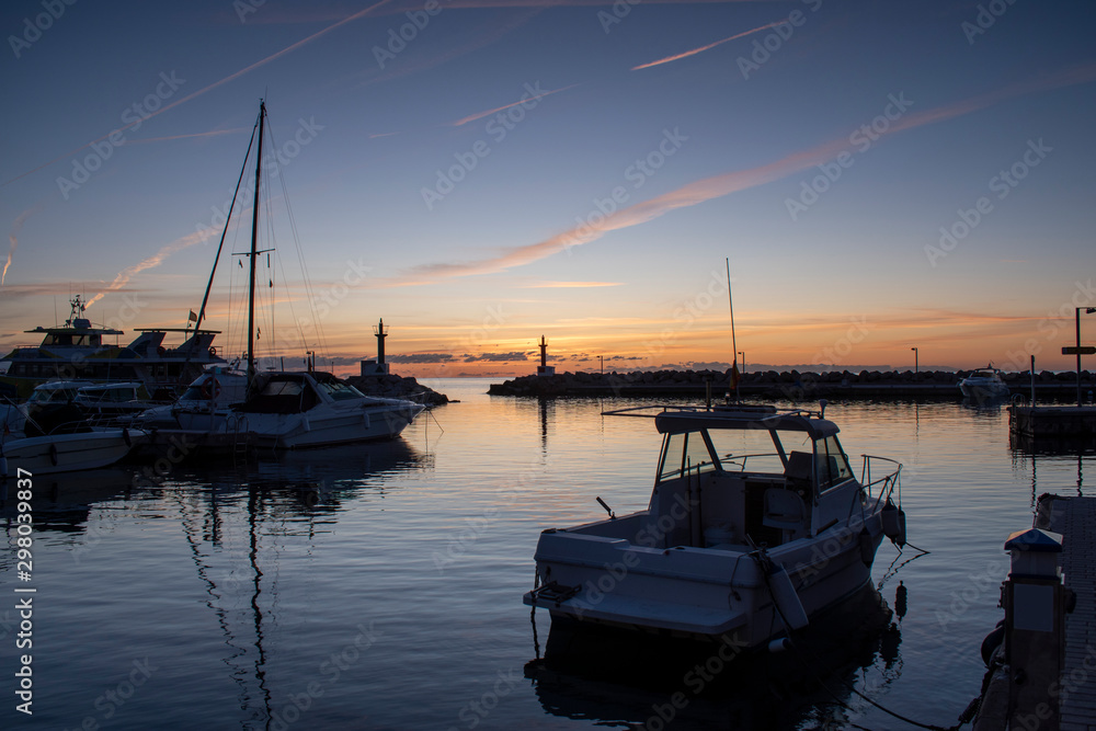 Fototapeta premium Sunrise over Cala Bona Majorca Marina with boats in the foreground of a beautiful array of vibrant and golden colours.