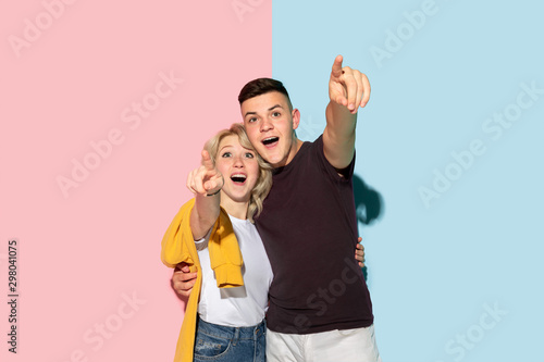 Young emotional man and woman in bright casual clothes posing on pink and blue background. Concept of human emotions, facial expession, relations, ad. Beautiful caucasian couple pointing and smiling.