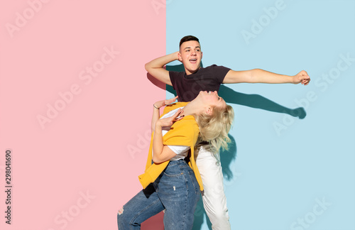 Young emotional man and woman in bright casual clothes posing on pink and blue background. Concept of human emotions, facial expession, relations, ad. Beautiful caucasian couple dancing together.