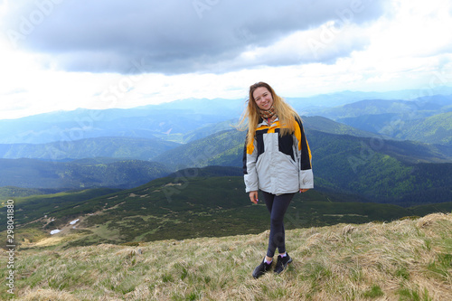 Young smiling female tourist wearing yellow jacket standing in Alps mountains. photo