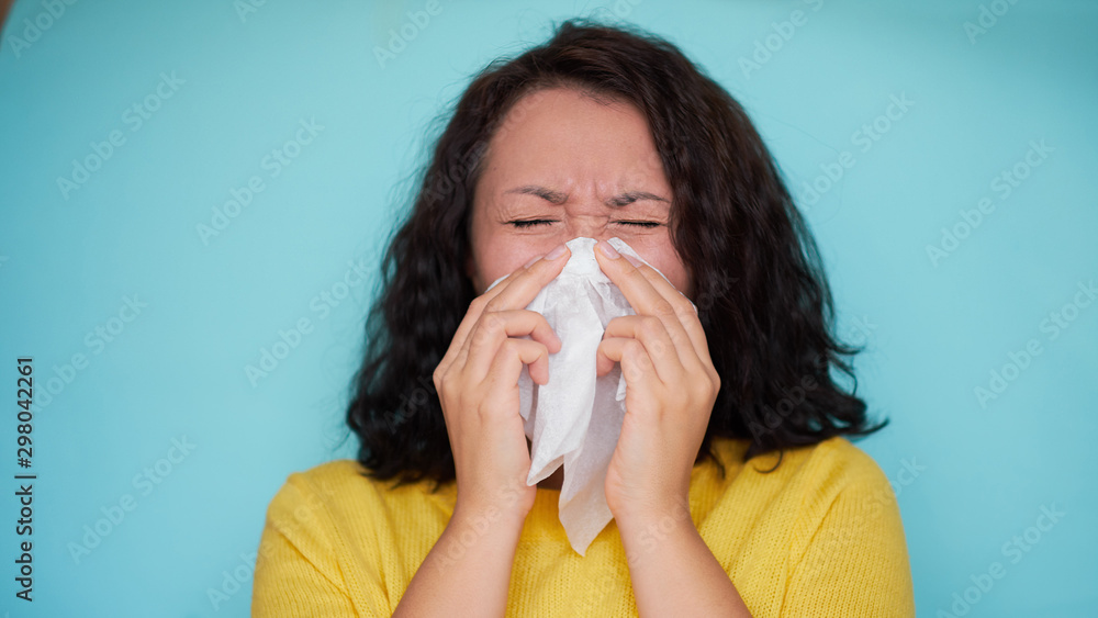 Burnette woman blowing nose into tissue. Flu cold or allergy symptom. Sick woman girl sneezing in tissue on blue. Health care. Burnette woman blowing nose into tissue. Flu cold or allergy symptom. Sick woman girl sneezing in tissue on blue. Health care.