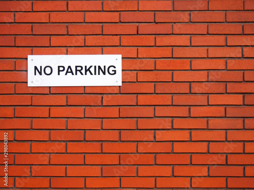 a white sign saying no parking on a red brick wall