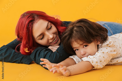 Image of cheerful woman and her daughter smiling and lying on floor