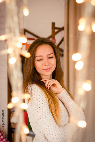 Young female person standing near yellow twinkling garlands in room. photo