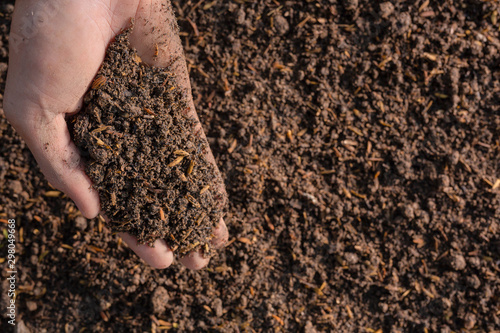 The hand of a man holding the soil in his hand and having a black earth background.