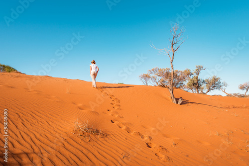 Woman walks on red sand dune in Australia  fiery red sand eroded from huge rock formation and a sanctuary for the Aboriginals