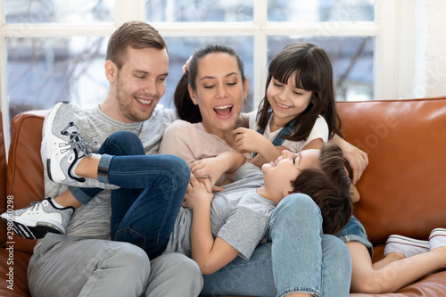 Overjoyed parents and smiling daughter tickling laughing son brother.