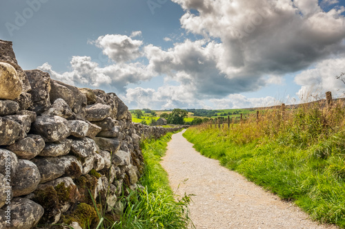 Fotografie Low level view of a very old, stone wall seen extending to an abandoned farmhouse in the distance