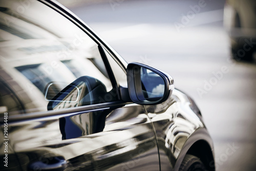 On a beautiful polished car that drives past the building, a rearview mirror reflecting the blue sky.