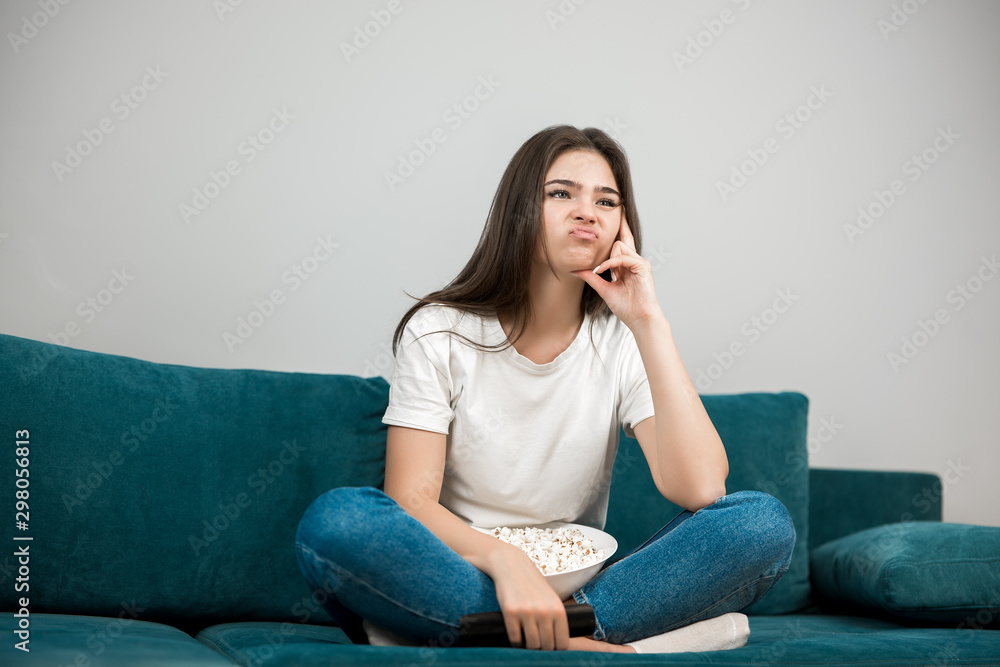 beautiful young woman cheers on her favorite team looking upset while watching football game eating popcorn on the sofa at home beautiful young woman cheers on her favorite team looking upset while watching football game eating popcorn on the sofa at home