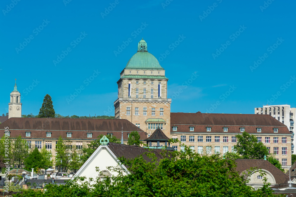 View of the historic center of Zurich at the bank of Limmat River, with beautiful house rooftops and main building of University Zurich, view form Lindenhof hill.