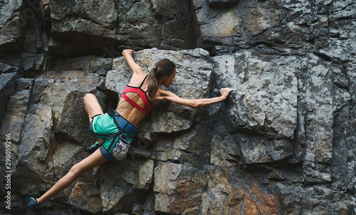 Sports woman with slim fit body climbing on the rock, having workout, climber makes a hard move.