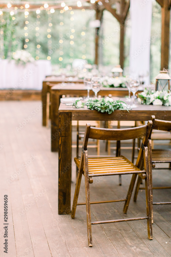Wedding tables in restaurant outdoors. Banquet. The chairs and table for guests, decorated with lanterns and flowers, served with cutlery and crockery. Restaurant outdoors in forest or garden