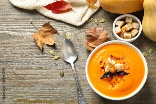 Delicious pumpkin soup in bowl on wooden table, flat lay. Space for text