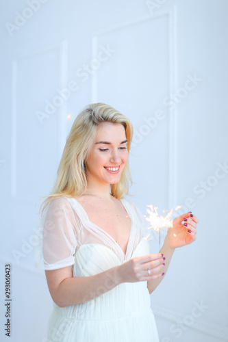 Blonde woman keeping bengal light and wearing white dress. photo