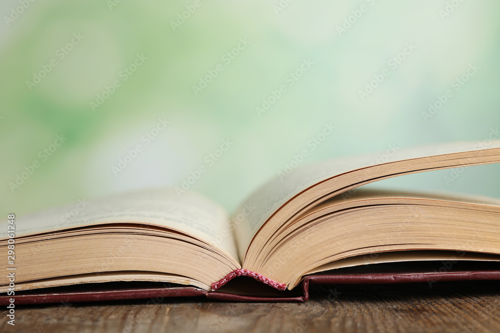 Open book on wooden table against blurred green background, closeup. Space for text Open book on wooden table against blurred green background, closeup. Space for text