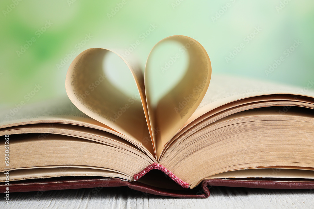 Open book on white wooden table against blurred green background, closeup Open book on white wooden table against blurred green background, closeup