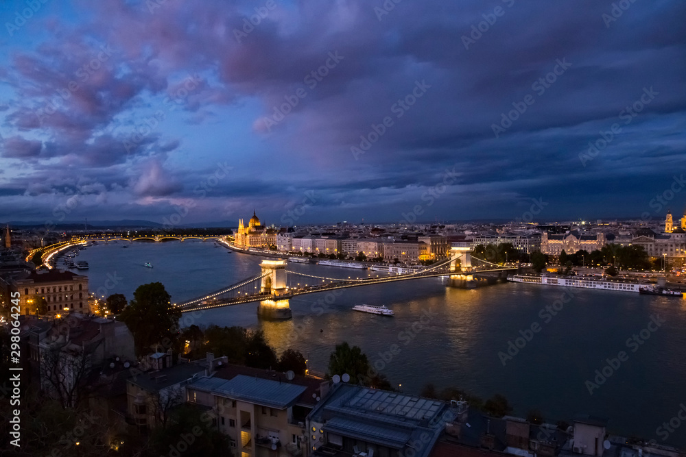 Night aerial panorama of Budapest with Chain Bridge and Parliament buliding and river boats on Danube river illuminated with night lights.