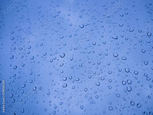 Rain drops on car window glasses surface, water drops with natural blue background.