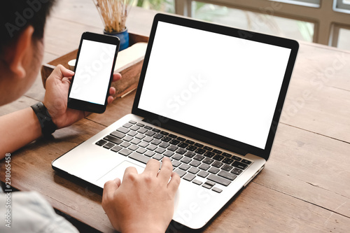 mockup image computer,cell phone blank screen for hand typing text,using laptop contact business searching information in workplace on desk at office.design creative work space on wooden desk
