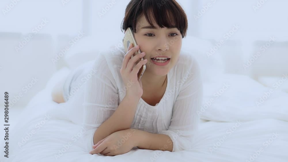 Beautiful young asian woman smiling lying relax in the bedroom, girl using mobile smart phone talking enjoy and fun, communication and social network concept, slow motion. Beautiful young asian woman smiling lying relax in the bedroom, girl using mobile smart phone talking enjoy and fun, communication and social network concept, slow motion.