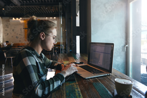 young woman freelancer or student working on laptop, sitting in cafe, drinking coffee