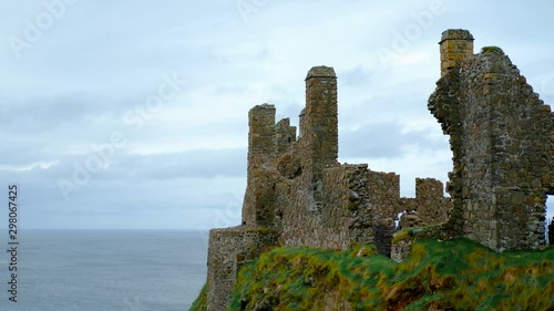 wide locked shot of the ruins of Dunluce Castle on a steep grassy cliff with a blue cloudy sky and a calm ocean in the background. Scenic background shot with copy space on the left side. photo