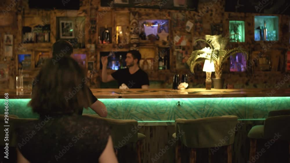 Rear view of group of young people of different ethnicities entering bar and sitting down at counter to have drinks and relax in the evening Rear view of group of young people of different ethnicities entering bar and sitting down at counter to have drinks and relax in the evening