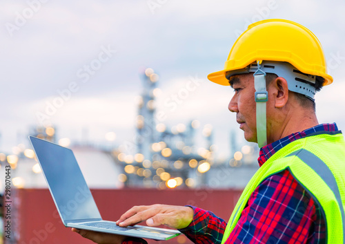 Male foreman in yellow safety helmet is looking to The computer in front of blurred background of refinery station © sutthichai