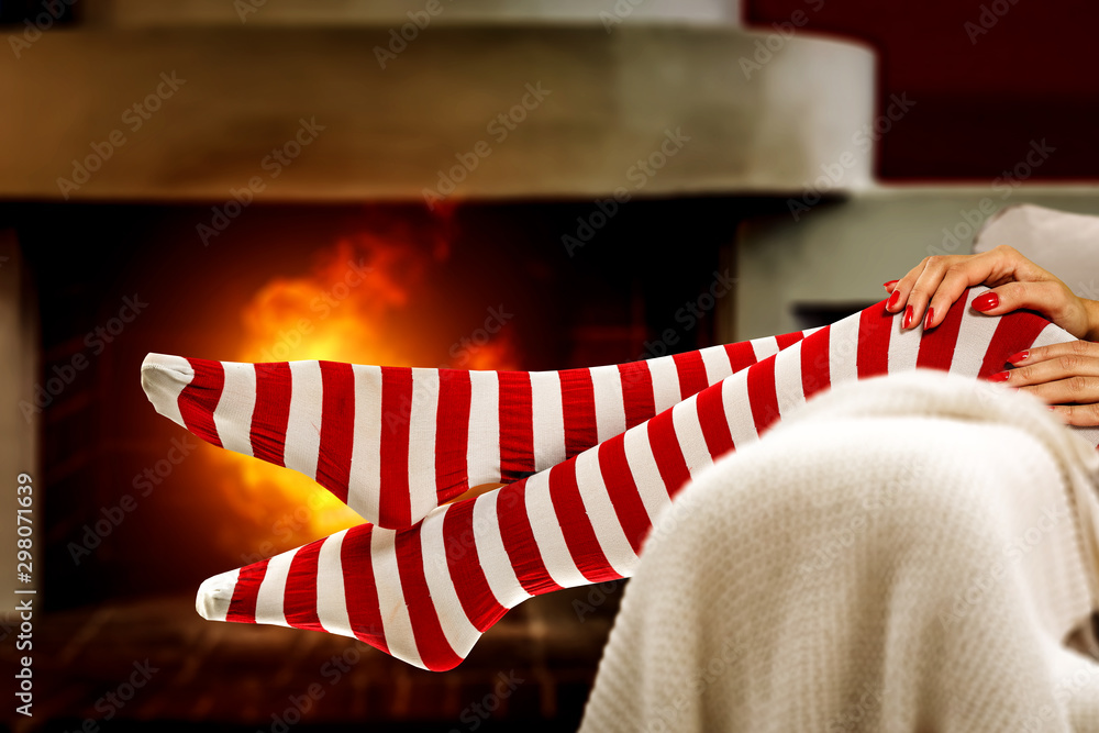 Woman legs with christmas socks and home interior with fireplace Woman legs with christmas socks and home interior with fireplace