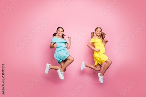 Full size profile photo of two friendship small sisters ladies models jumping high hurry home summer holidays wear blue yellow dresses isolated pink color background