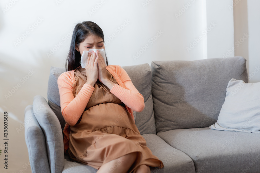 Young Asian pregnant woman have suffering from flu and sneeze, runny nose, stuffy nose and then her blow nose using a tissue Young Asian pregnant woman have suffering from flu and sneeze, runny nose, stuffy nose and then her blow nose using a tissue