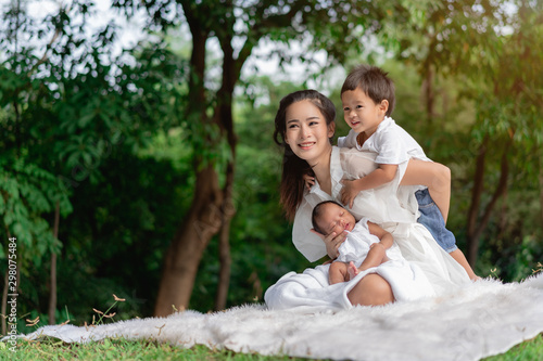 Happy loving family. Asian beautiful mother and her children, new born baby girl and a boy sitting on lawn to playing and hugging in the park