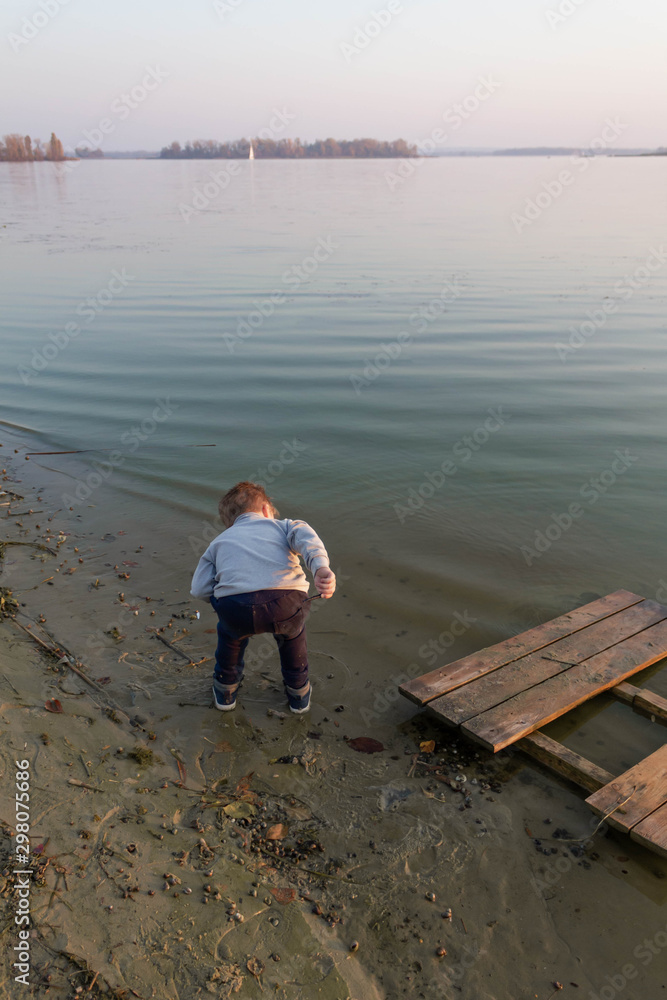 Little kid boy on a wooden pier on a lake, a river looks into the distance at the horizon Little kid boy on a wooden pier on a lake, a river looks into the distance at the horizon
