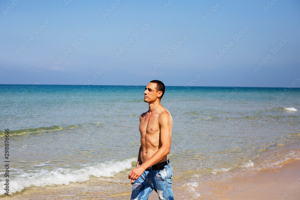 young muscular man resting and posing on the beach. A young man walks by the sea young muscular man resting and posing on the beach. A young man walks by the sea