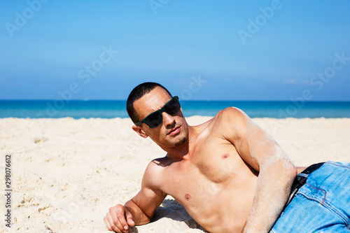 young muscular man resting and posing on the beach. 