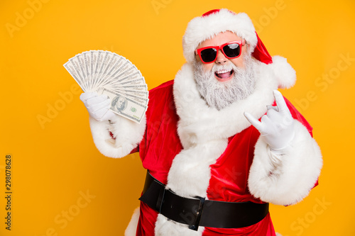 X-mas lottery win credit bank present for noel. Funky crazy hipster white bearded santa claus hold money fan show horned symbol enjoy deposit gift wear red hat isolated yellow color background photo