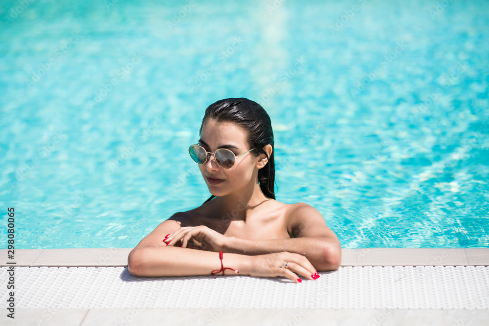 Beautiful young woman in bikini and sunglasses relaxing at the swimming pool