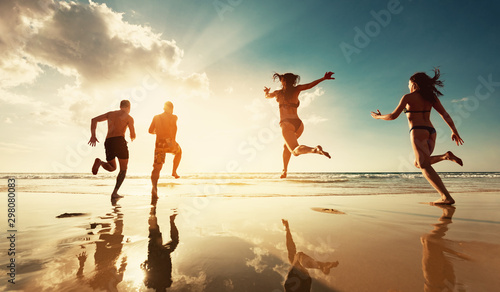 Four friends runs at sunset sea beach
