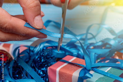 Hands wrapping gift on the background of wrapping paper and satin ribbons. Holidays preparations concept.