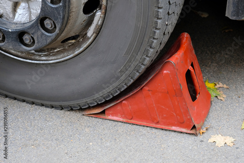 Red wheel chock under the wheel of a car close-up. Car repair. Metal rack for machine repair. photo