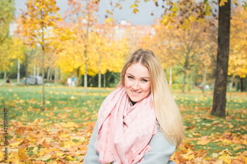 Autumn portrait in the park with yellow leaves of a beautiful blonde girl in warm clothes and a pink scarf around her neck