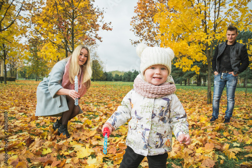 Dad mom and a little two-year-old daughter are playing in the autumn park against the background of yellow foliage