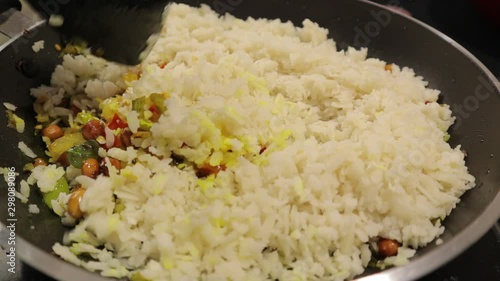 Preparing Fresh South Indian breakfast or snacks Poha, Mixing Raw Poha or flattened rice with veggies and ingredients in frying pan. photo