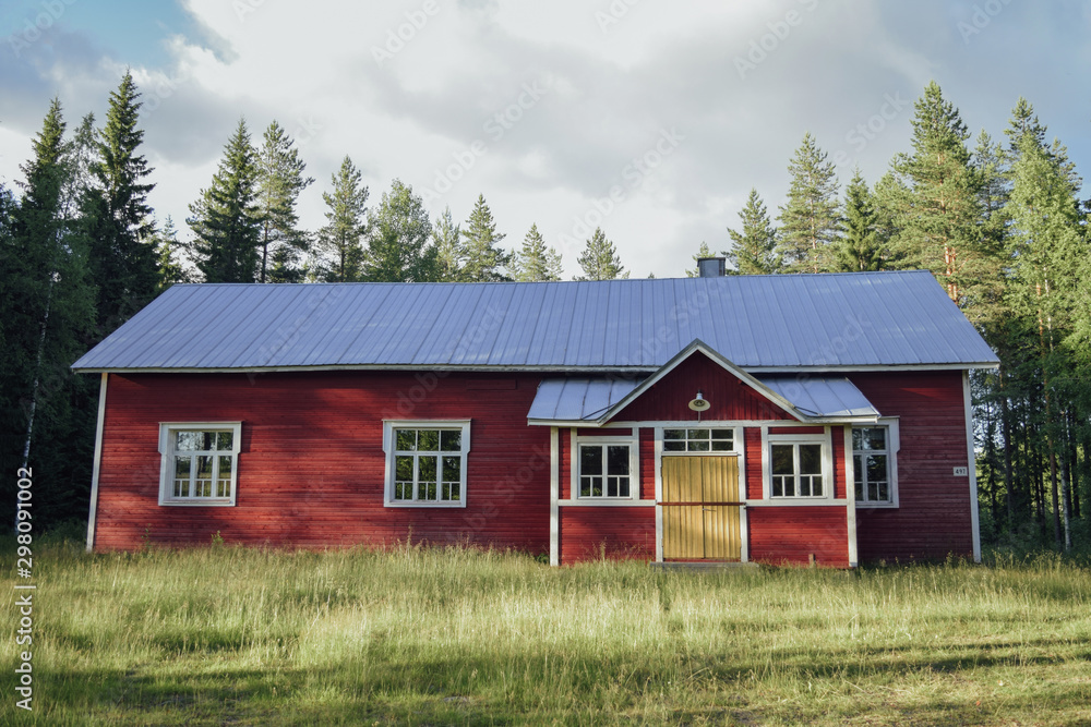 Red farm house in the forest at finnish countryside summer sunny day, green grass and coniferouse tree