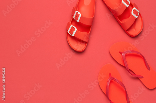 Fashionable beach coral flip flops and sandals on bright coral background. Flat lay, top view, copy space. Creative beach concept, stylish summer shoes, vacation, travel. Trend coral color