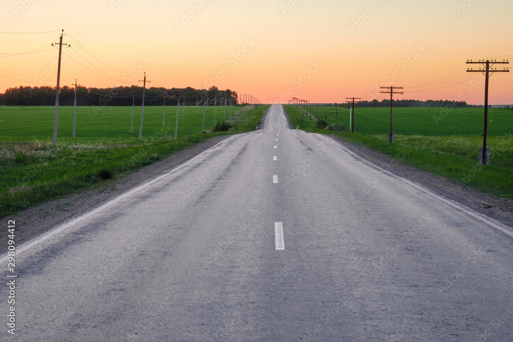 sunset sky and asphalt road rising up along the road pillars and growing grass sunset sky and asphalt road rising up along the road pillars and growing grass