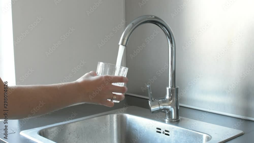 Hands in the kitchen taking a glass of water at the kitchen sink at home Hands in the kitchen taking a glass of water at the kitchen sink at home