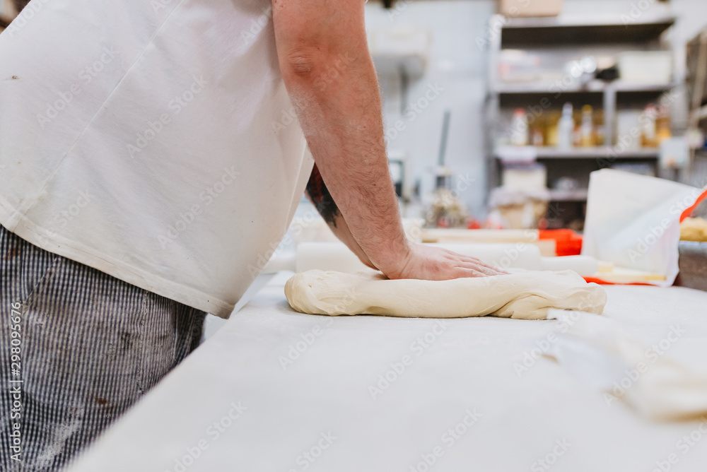 Side view of crop overweight man in uniform kneading soft dough on table while working in bakery kitchen Side view of crop overweight man in uniform kneading soft dough on table while working in bakery kitchen